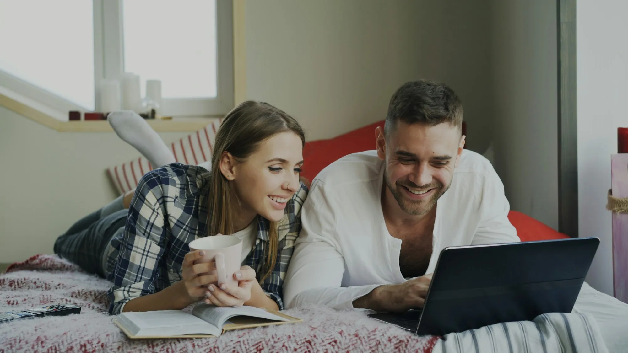 Couple lying on a bed looking at a laptop while comparing group life insurance from work with an individual policy in Northbrook