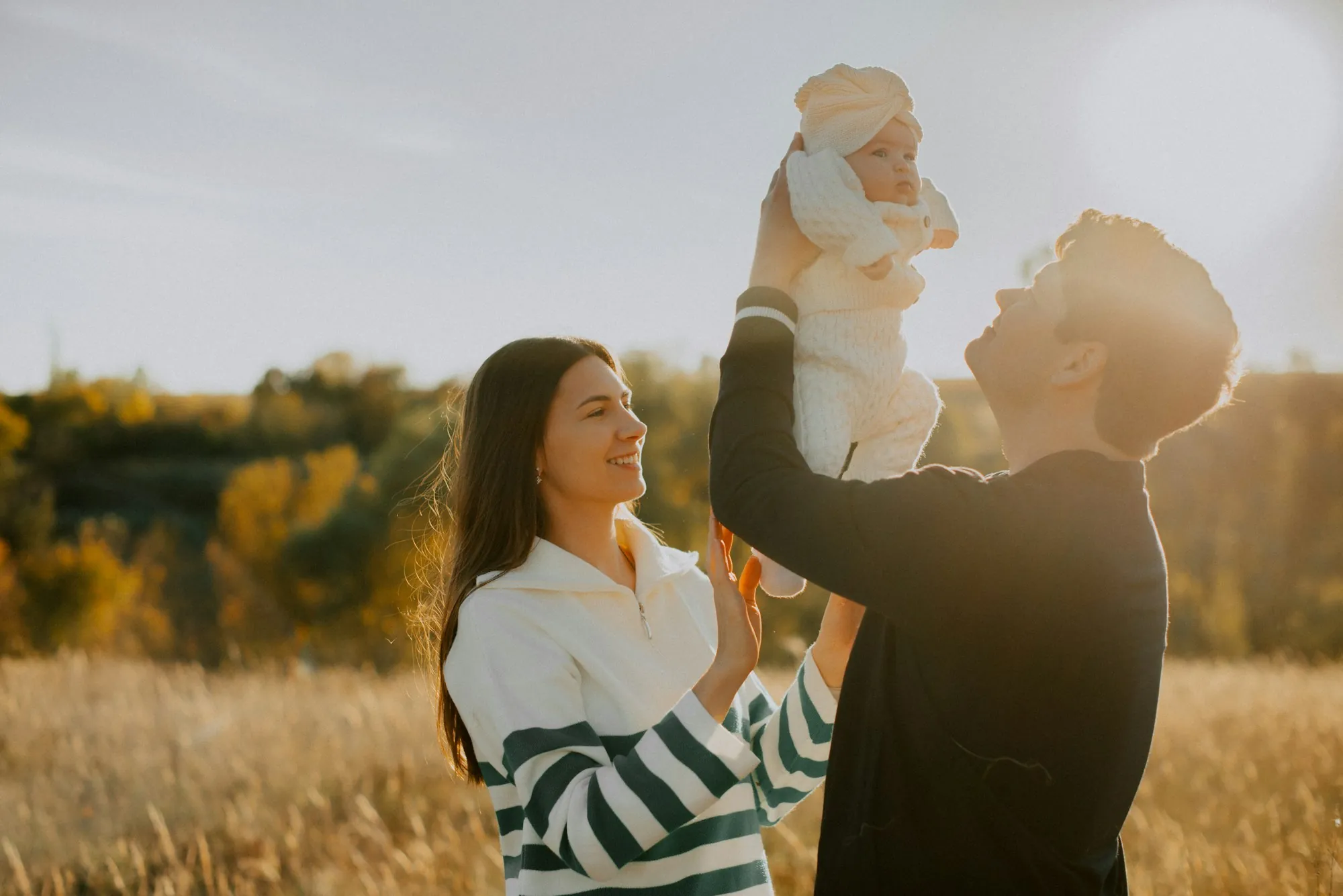 Parents lifting their baby toward the sky in a wheat field