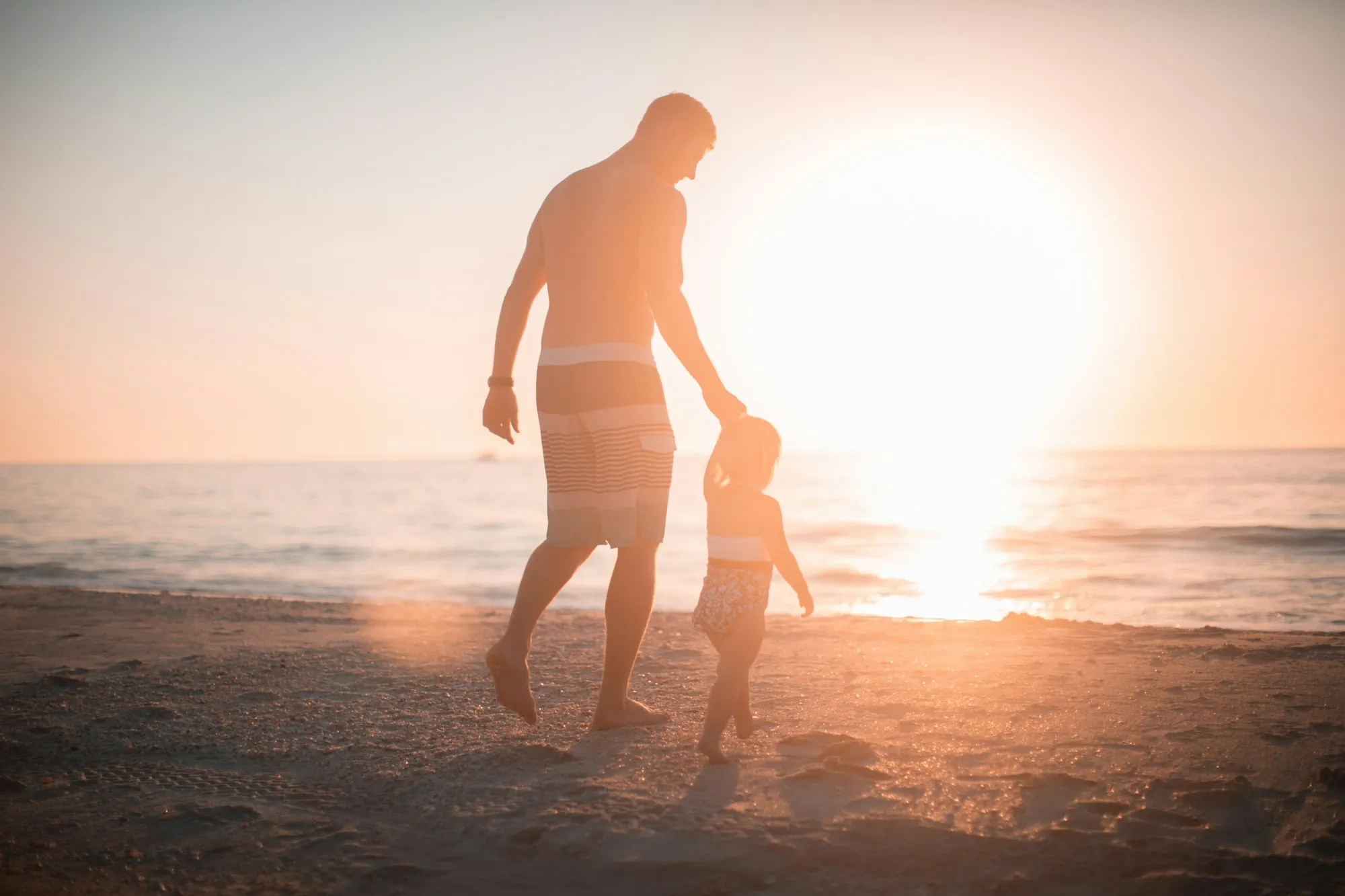Parent and child walking along the shore at sunset